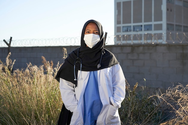 Un giovane medico musulmano con un velo all'aperto. Un medico islamico con l'hijab è in piedi fuori in una zona povera di fronte alla telecamera. Medici volontari.