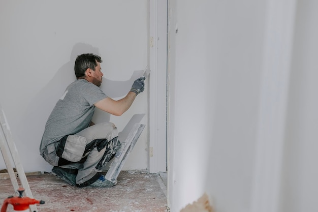 Un giovane muratore sta intonacando una porta