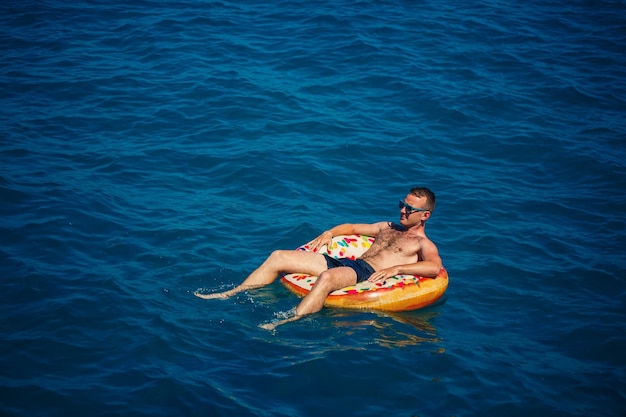 Un giovane nuota in mare aperto su un anello gonfiabile in una giornata di sole Vacanze estive in vacanza