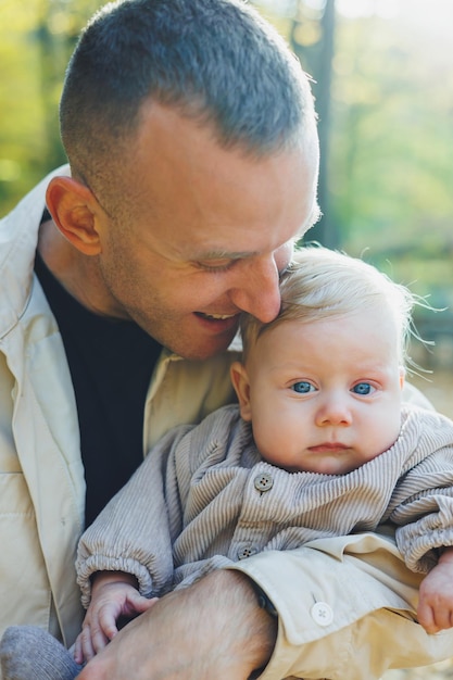 Un giovane padre felice abbraccia il suo piccolo figlio al sole in una calda giornata primaverile o estiva nel parco La luce del sole nel parco Padre e figlio concetto di famiglia in natura