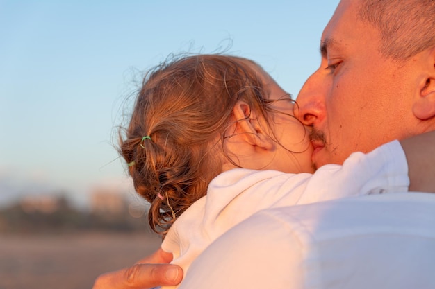 Un giovane papà con una figlia piccola cammina lungo la spiaggia del mare al tramonto