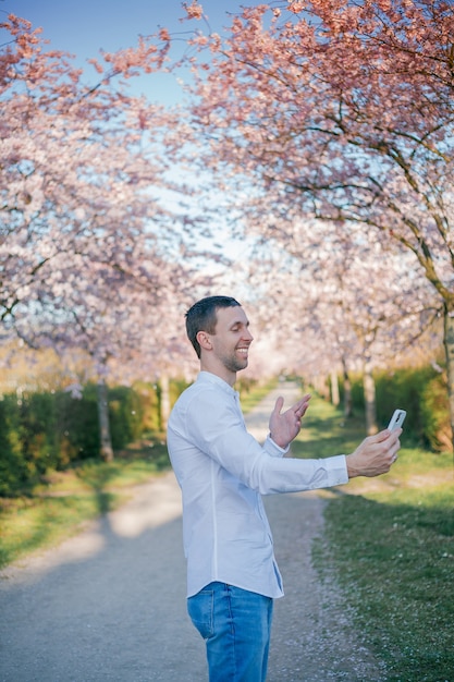 Un giovane parla al telefono di un giardino in fiore di sakura. Primavera.