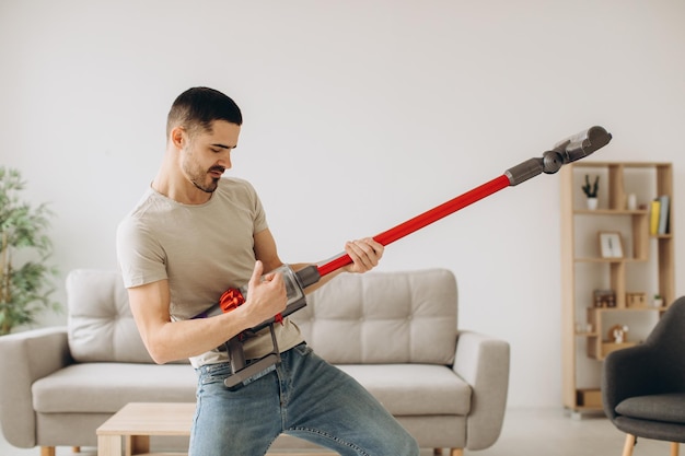 Un giovane positivo pulisce la stanza e tiene in mano un aspirapolvere come una chitarra