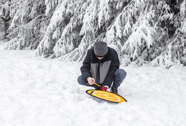 Un giovane prepara una piattaforma per un drone in una foresta invernale