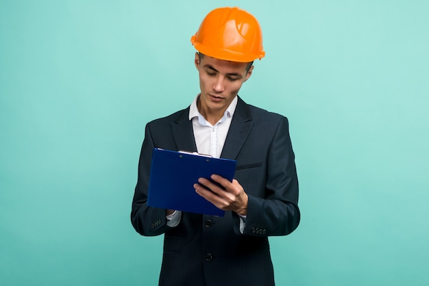 Un giovane professionista che indossa un cappello duro e portando un blocco per appunti su sfondo blu