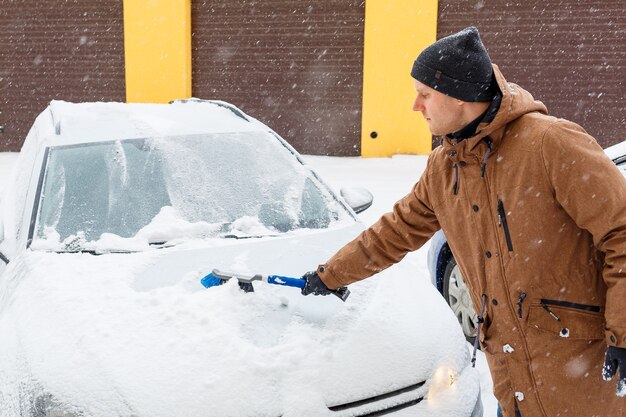 Un giovane pulisce la neve dalla sua auto. Cura dell'auto in inverno