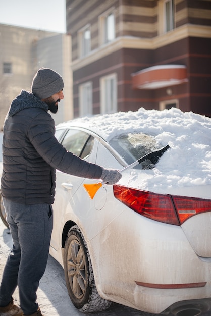 Un giovane pulisce la sua auto dopo una nevicata in una soleggiata giornata gelida.