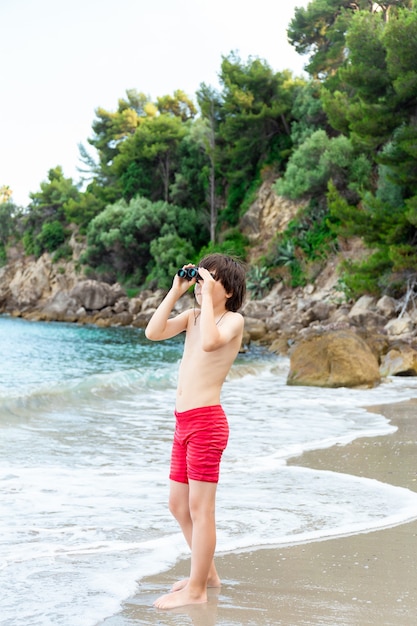 Un giovane ragazzo che guarda attraverso il binocolo che soggiornano in riva al mare sulla spiaggia.