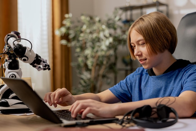Un giovane ragazzo con lunghi capelli biondi siede su una sedia a una scrivania che lavora su un computer portatile su un software