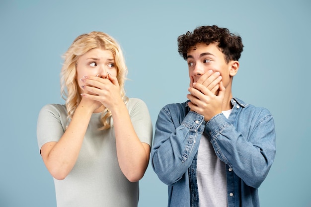Un giovane ragazzo e una ragazza spaventati si coprono la bocca con le mani e si guardano.