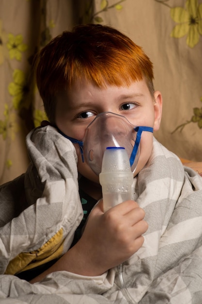 Un giovane ragazzo respira attraverso un inalatore a letto Bambino avvolto in una coperta Trattamento della bronchite polmonite concetto di coronavirus
