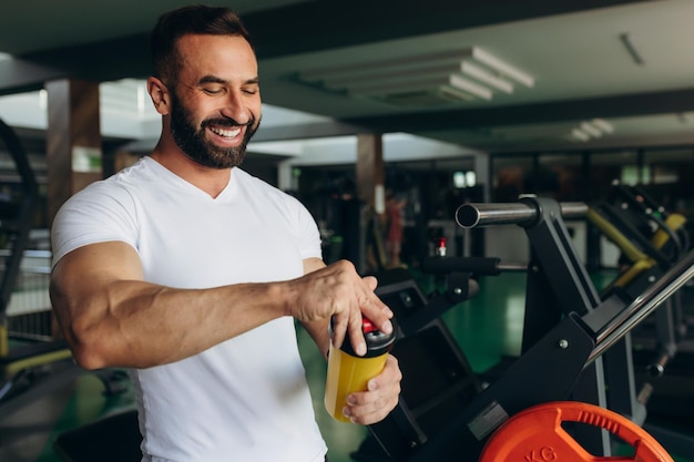 Un giovane riposa dopo l'allenamento in palestra tenendo uno shaker in mano Concetto di fitness e allenamento