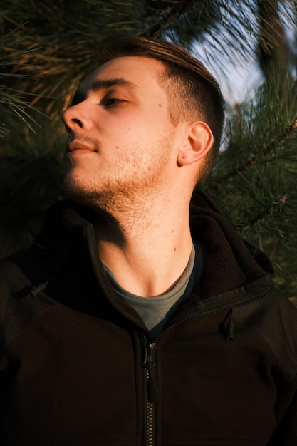 Un giovane ritratto con i capelli grigi cammina attraverso una foresta e gode di uno stile di vita sano Ragazzo attraente e bello in giacca nera che posa in pino e luci del tramonto
