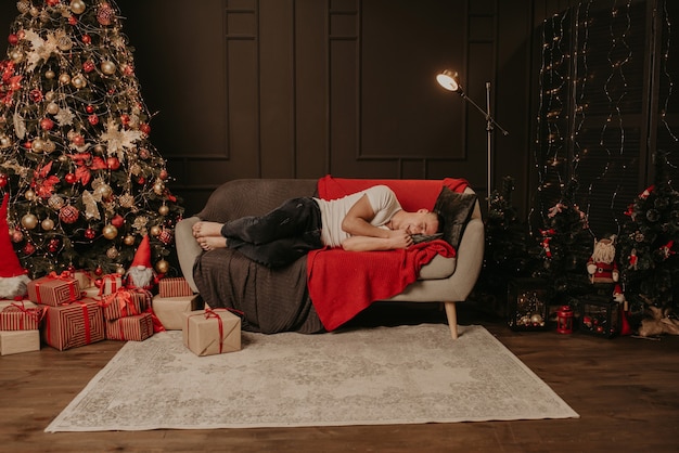 Un giovane si è addormentato sul divano vicino all'albero di Natale. casa decorata per il nuovo anno