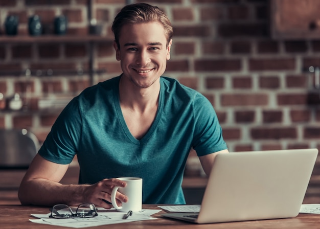 Un giovane si siede a un tavolo in ufficio e lavora al computer. Bruna si siede a un computer e lavora con una tazza di caffè in mano.