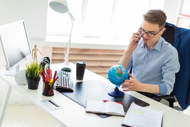 Un giovane si siede in ufficio alla scrivania di un computer, parlando al telefono e guardando il globo.