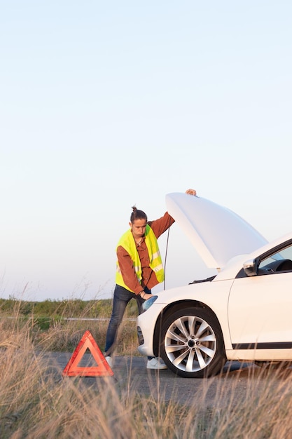 Un giovane sopraffatto con la sua auto in bisogno di riparazione in mezzo al nulla in campagna