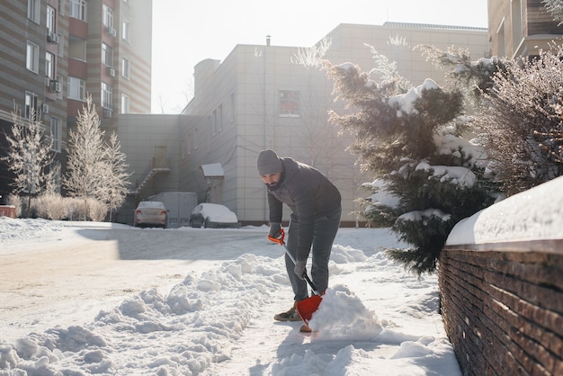 Un giovane spazza la neve davanti alla casa in una giornata di sole e gelo. Pulire la strada dalla neve.