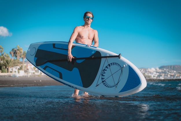 Un giovane sportivo pratica il paddle surf sulla spiaggia sotto un cielo blu