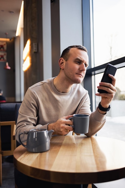 Un giovane sta mandando messaggi dal suo cellulare in un bar e beve un cappuccino Giovane uomo alla moda che beve un caffè espresso in un caffè della città durante il pranzo e il lavoro