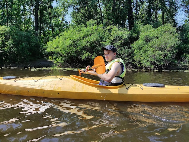 Un giovane sta nuotando in un kayak con una pagaia in un giubbotto di salvataggio sul fiume