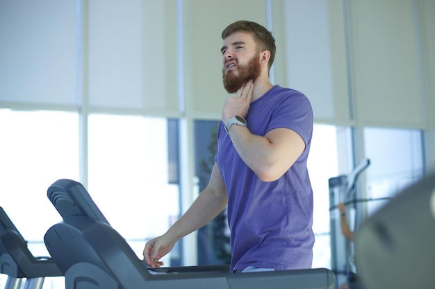 Un giovane stanco e esausto si sta allenando, corre sul tapis roulant in palestra, si sente male, non è in salute.