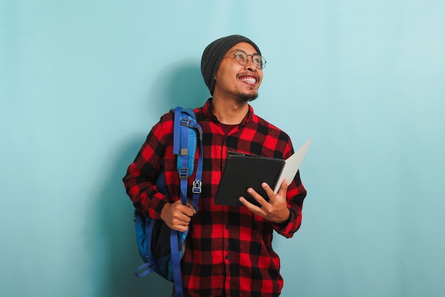 Un giovane studente asiatico che indossa uno zaino tiene in mano dei libri mentre si trova su uno sfondo blu