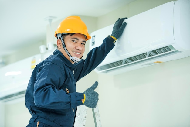 Un giovane tecnico asiatico che indossa un'uniforme blu che controllaInstallatore di condizionatori d'aria professionale che mantiene lo spazio moderno del condizionatore d'aria per interni per il testo