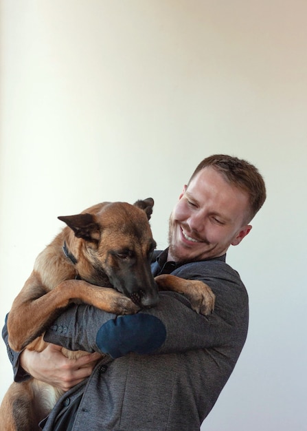 Un giovane tiene in braccio un cane da pastore belga Malinois e sorride.