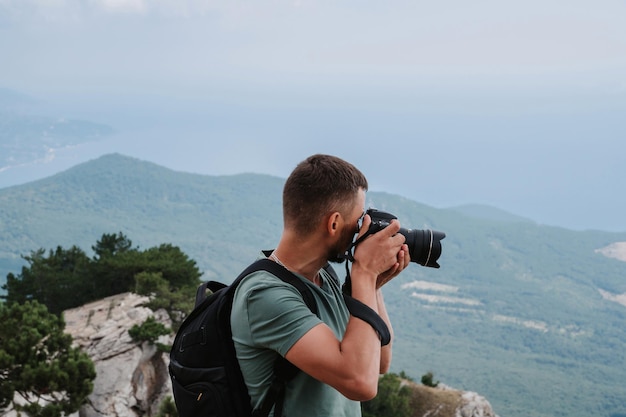 Un giovane turista maschio con uno zaino è salito in cima alla montagna e scatta foto sulla cima da un'altezza Il concetto di vita attiva ed escursionismo