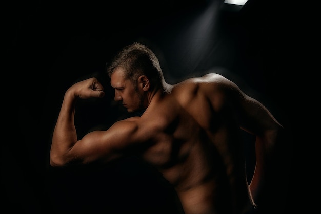 Un giovane uomo abbronzato di corporatura atletica, un istruttore di fitness fa esercizi in palestra. Vista dal bac