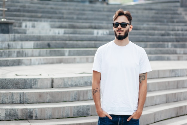 Un giovane uomo alla moda con la barba in maglietta bianca e occhiali