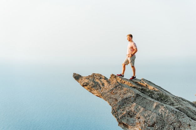 Un giovane uomo atletico si erge su una pittoresca scogliera ripida sopra il mare contro il cielo