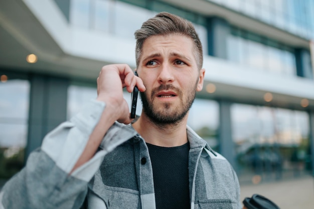 Un giovane uomo barbuto appare turbato mentre è impegnato in una conversazione telefonica in città con un uomo arrabbiato