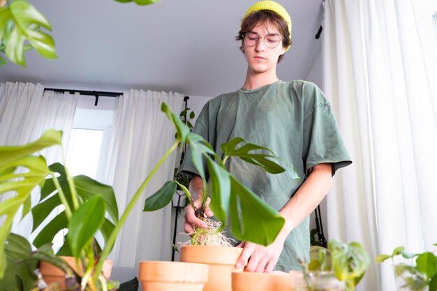 Un giovane uomo bello con i capelli lunghi scuri che indossa una maglietta verde tiene una pianta d'appartamento nelle mani Ampel pianta di arrampicata vaso d'argilla Monstera