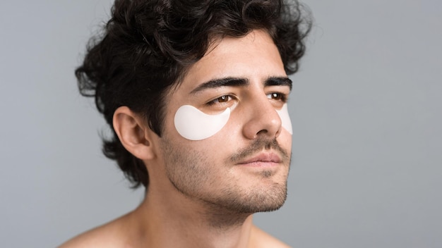 Un giovane uomo caucasico con barba ispida che si mette delle toppe sotto gli occhi