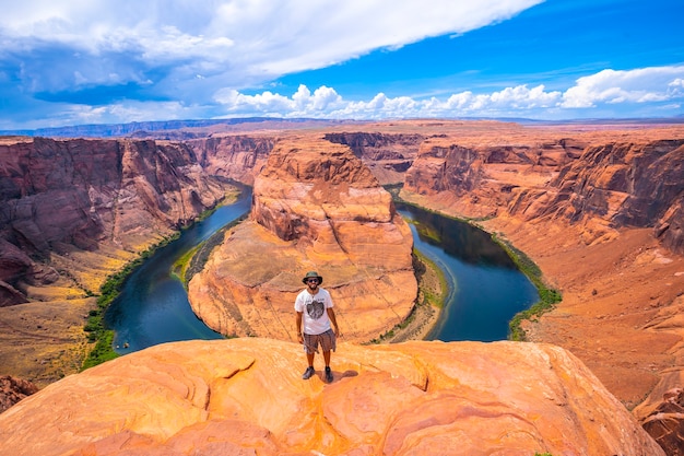 Un giovane uomo con camicia bianca, cappello verde e guardando la fotocamera a Horseshoe Bend e il fiume Colorado in background, Arizona. stati Uniti