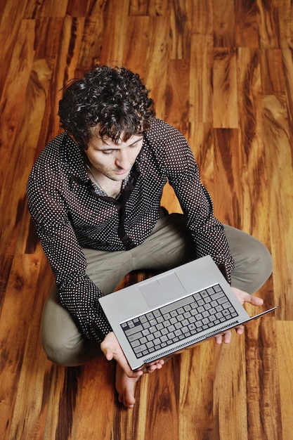 Un giovane uomo con un computer portatile sullo sfondo del pavimento in legno