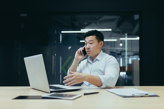 Un giovane uomo d'affari asiatico risolve i problemi di lavoro parla al telefono a cui è seduto un uomo preoccupato