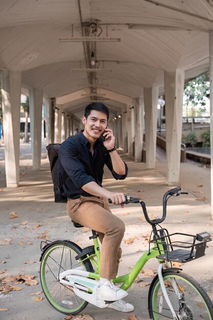 Un giovane uomo d'affari asiatico va a lavoro in bicicletta in piedi fuori dall'ufficio a parlare al telefono