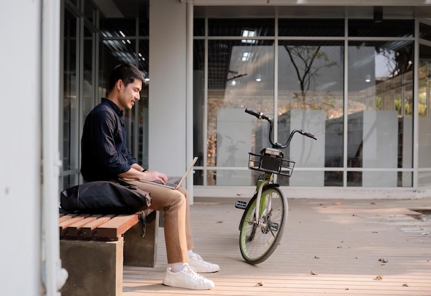 Un giovane uomo d'affari asiatico va a lavoro in bicicletta usando una bottiglia d'acqua riutilizzabile che lavora fuori dal