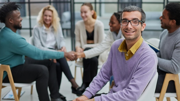 Un giovane uomo d'affari felice con un maglione viola siede sullo sfondo dei suoi colleghi