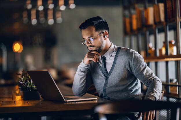 Un giovane uomo d'affari serio è seduto in un bar e ha una riunione online sul laptop