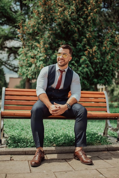 Un giovane uomo d'affari sexy in un vestito seduto nel parco in pausa di lavoro