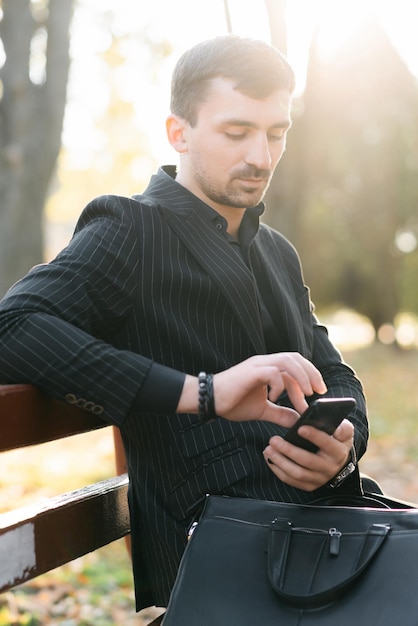 Un giovane uomo d'affari sta scrivendo ai suoi clienti seduti su una panchina nel parco