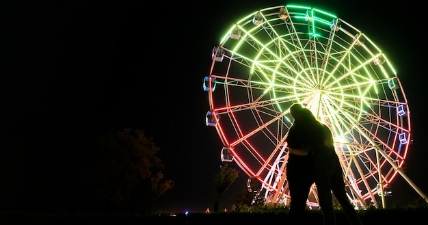 Un giovane uomo e una donna si innamorano di notte nel parco divertimenti vicino alla ruota panoramica