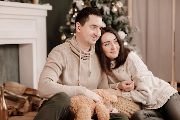 Un giovane uomo e una ragazza che si amano si abbracciano in comodi maglioni vicino a un albero di Natale a casa