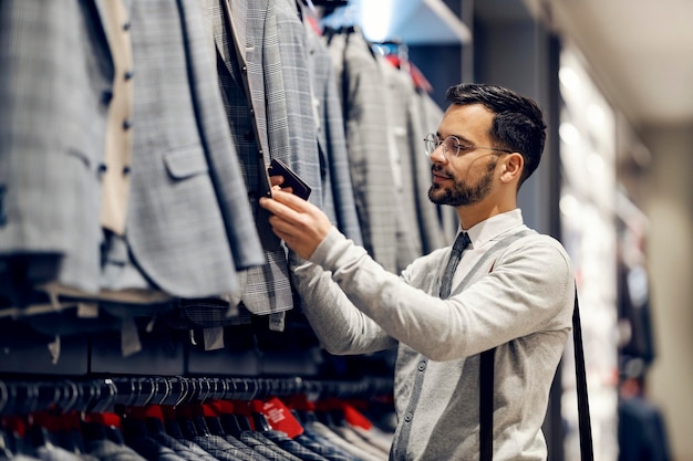 Un giovane uomo elegante è in piedi in un negozio di abbigliamento e cerca un abito adatto