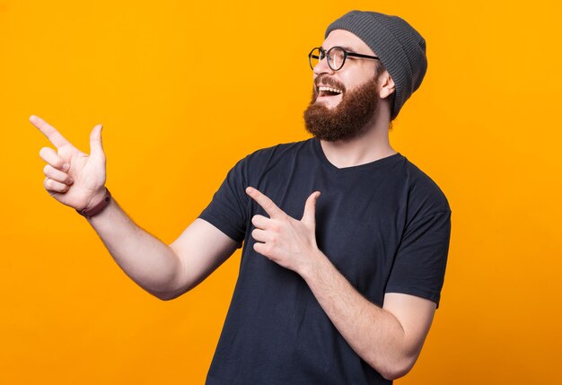 Un giovane uomo felice con la barba sorride e indica uno spazio libero con le dita