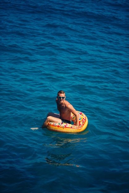 Un giovane uomo galleggia su un cerchio gonfiabile dell'anello d'aria nel mare con acqua blu Vacanza festiva in una felice giornata di sole Concetto di vacanza vista dall'alto